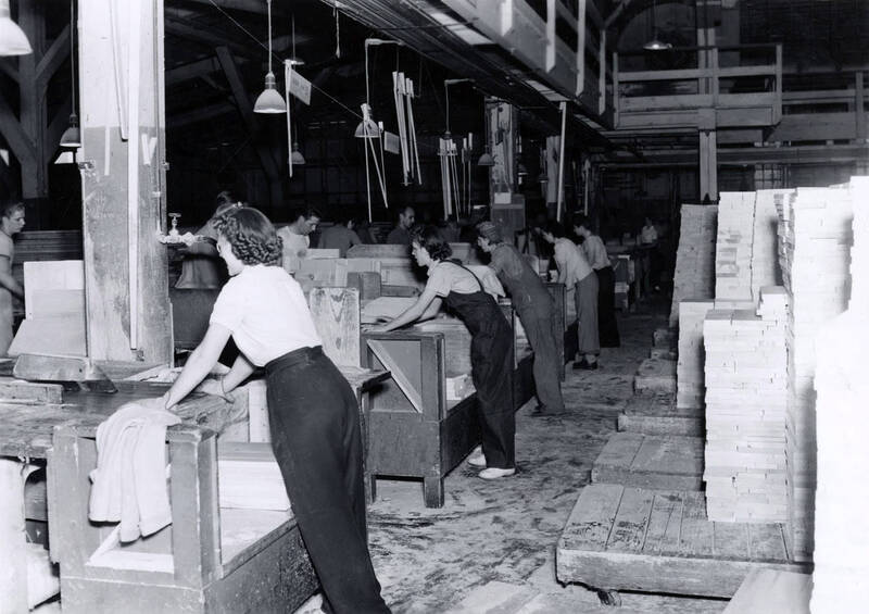 women working at the Clearwater Sawmill and Lumber factory sawing boards and loading cut boards from a conveyor belt