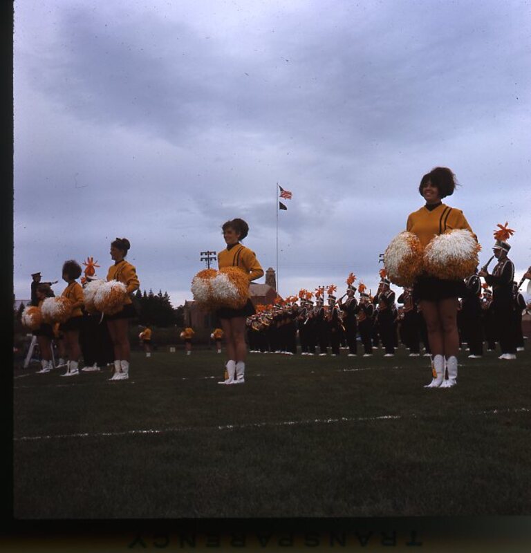 cheerleaders performing on field with band during halftime at Homecoming football game